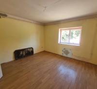 A room in a family house with a wooden floor, a simple ceiling, and a window facing the yard.
