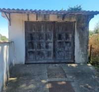An older garage behind a family house in Ipolyvece with a metal roof and wooden doors.
