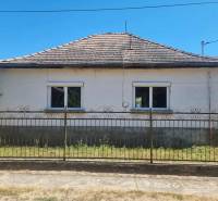 A family house in Ipolyvec with two windows and a sloping roof behind a metal fence.