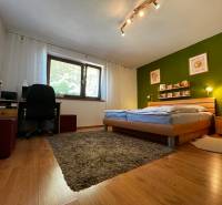 Bedroom in a family house with a wooden bed, green wall, and a work corner.