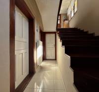 A hallway with a staircase and wooden details in a family house, entrance to a room with white doors.