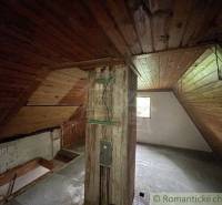 Attic in a family house with wooden paneling and a beam, illuminated by a window.