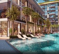 Apartment construction in Pattaya with a pool and loungers surrounded by palm trees and plants.
