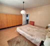 Bedroom in a family house with a bed, wardrobe, and chair on a light floor.