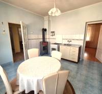 A kitchen in a family house with a table, chairs, a stove, and a tiled stove.