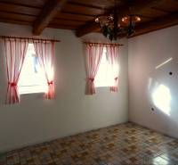 A room in a family house with a ceramic floor, wooden ceiling, and decorative curtains.