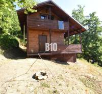 A wooden cabin in nature near Bytča, surrounded by trees and a fire pit.
