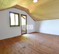 Attic spaces of the cottage with wooden floor and ceiling, window and door to the terrace.