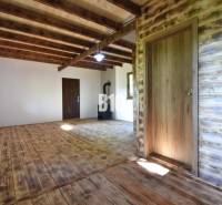 Interior of a cabin with wooden beams, flooring, and a stove for heating.