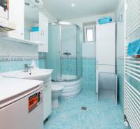 A bathroom with a washing machine and a shower in a 2-room apartment. Light tiles.