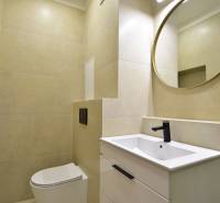 Bathroom in a 2-room apartment with a toilet, sink, black faucet, and round mirror.