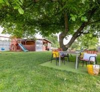 The garden of a family house in Ploské with a play set and outdoor seating under a tree.