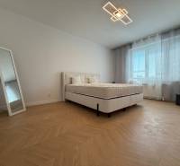 A bedroom in a 3-room apartment with a bed, a mirror, and a large window with blinds.