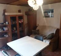 The interior of a cabin with simple furniture, a table, chairs, and an armchair under a chandelier.