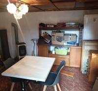 Small table, chairs, wardrobe, refrigerator, fireplace, shelves with items.