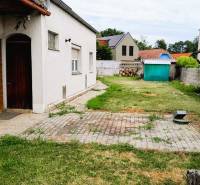 The courtyard of a family house in Potzneusiedl with a lawn, a garden shed, and a church tower in the background.