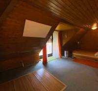 An attic room in a family house with wooden paneling and a bed on the right side.
