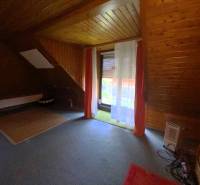 Attic room with wooden paneling in a family house, curtains over the window.