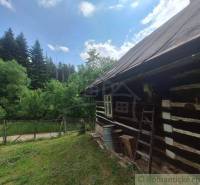 A cottage in Zákopčí surrounded by forest, wooden walls, a fence, and a blue sky.