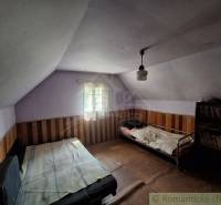 A room in a cabin with beds and a shelf full of books, wooden wall paneling.