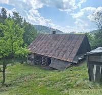 A wooden cabin in Zákopčie on a slope, surrounded by trees and a blue sky.