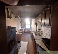 A kitchen in a cabin with wooden paneling, a tiled stove, and a sink.