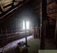 The attic of the cottage with wooden beams and a window illuminating the space.