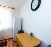 Dining table and refrigerator in a 2-room apartment with wall clock.