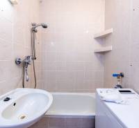 Bathroom in a 2-room apartment with a bathtub, sink, and washing machine, white tiles.