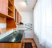 A kitchen unit with a white curtain and wooden cabinets in a 2-room apartment.