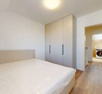 A bedroom in a family house with a bed, a wardrobe, and a view of the washing machine in the bathroom.