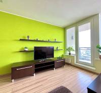 Living room of a two-room apartment with a colored wall and a television on a wooden cabinet.