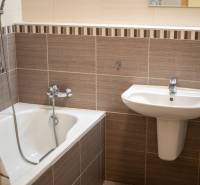 A bathroom with a sink and a bathtub in a 3-room apartment, with subtle wall tiles.