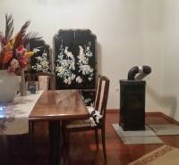 Interior of a family house with a wooden table, a tiled stove, and a decorative screen.