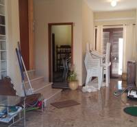 A hallway in a family house with stacked chairs, a glass table, and a vacuum cleaner.