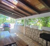 Covered terrace with a wooden table and grill in a family house in Vrsi.