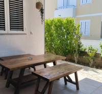A wooden table with benches on the terrace of a family house in Vrsi, surrounded by greenery.