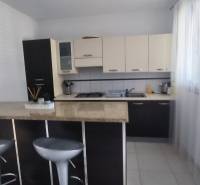 A kitchen in a family house with a bar counter, stools, and light cabinets.