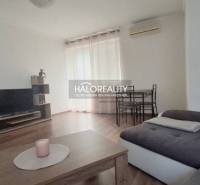 A living room in a two-room apartment with a sofa, a table, and a television on the floor.