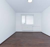 A room with white walls, a dark floor, and a window in a 3-room apartment.