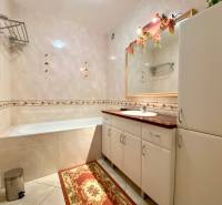 A bathroom in a 3-room apartment with a bathtub, cabinets, and a mirror with flowers.