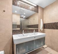 A bathroom with a double sink, brown tiles, and a mirror in a family house.