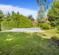 The garden of a family house on Malokarpatská Street in Limbach with a covered swimming pool surrounded by trees.