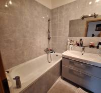 A bathroom in a 3-room apartment with a bathtub, sink, and gray tiles.