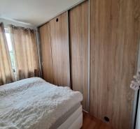 Bedroom in a 3-room apartment with a large built-in wardrobe and curtains on the windows.