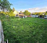 A plot of land by a family house in Kuzmice with trees and a lawn, fenced with a rustic fence.