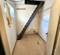 A narrow hallway with a metal ladder, a coat rack, and white walls in a family house.