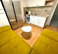 Living room in a studio apartment with a kitchenette, a yellow sofa, and modern appliances.