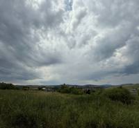 Cloudy sky over green commercial lands in Ľubotín with a visible horizon.