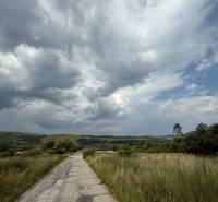 A country road leading through green fields in Ľubotín under a dramatic sky.